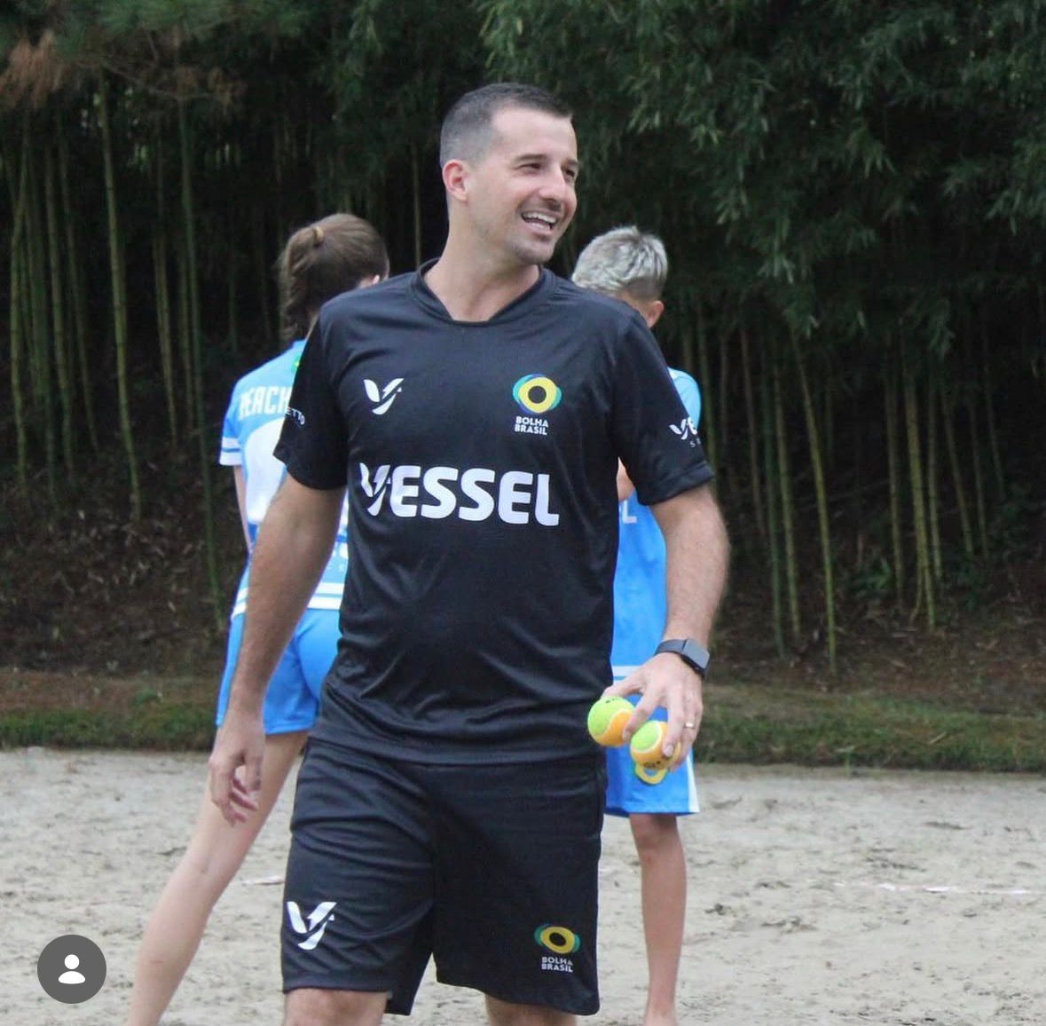 Head coach sorrindo durante treino na quadra de areia